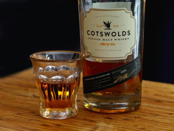 A close-up shot of Cotswolds single malt whisky bottle with a filled glass on a wooden table, showcasing elegance.