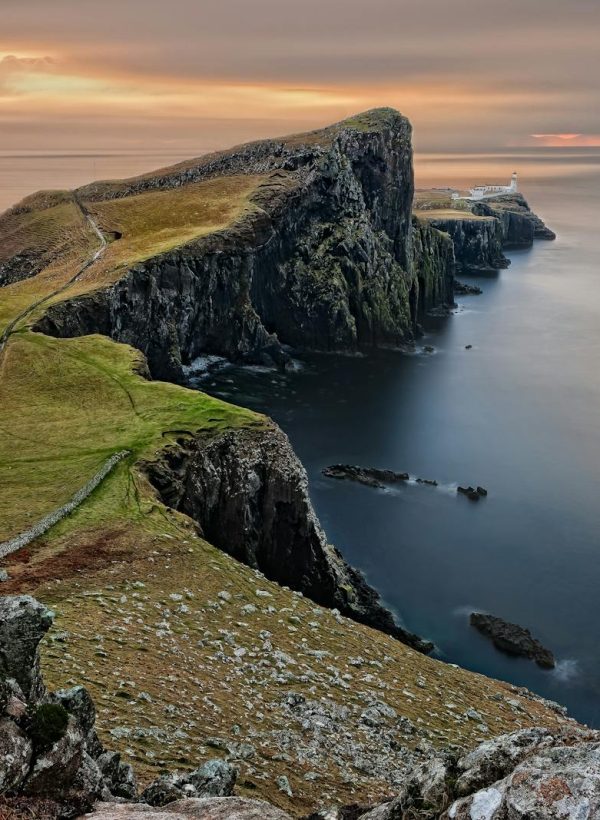 A stunning sunset view of Neist Point Lighthouse with cliffs and serene sea in Scotland.